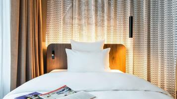 A hotel room with a neatly made bed, a magazine on the bed, and curtains with a pattern.