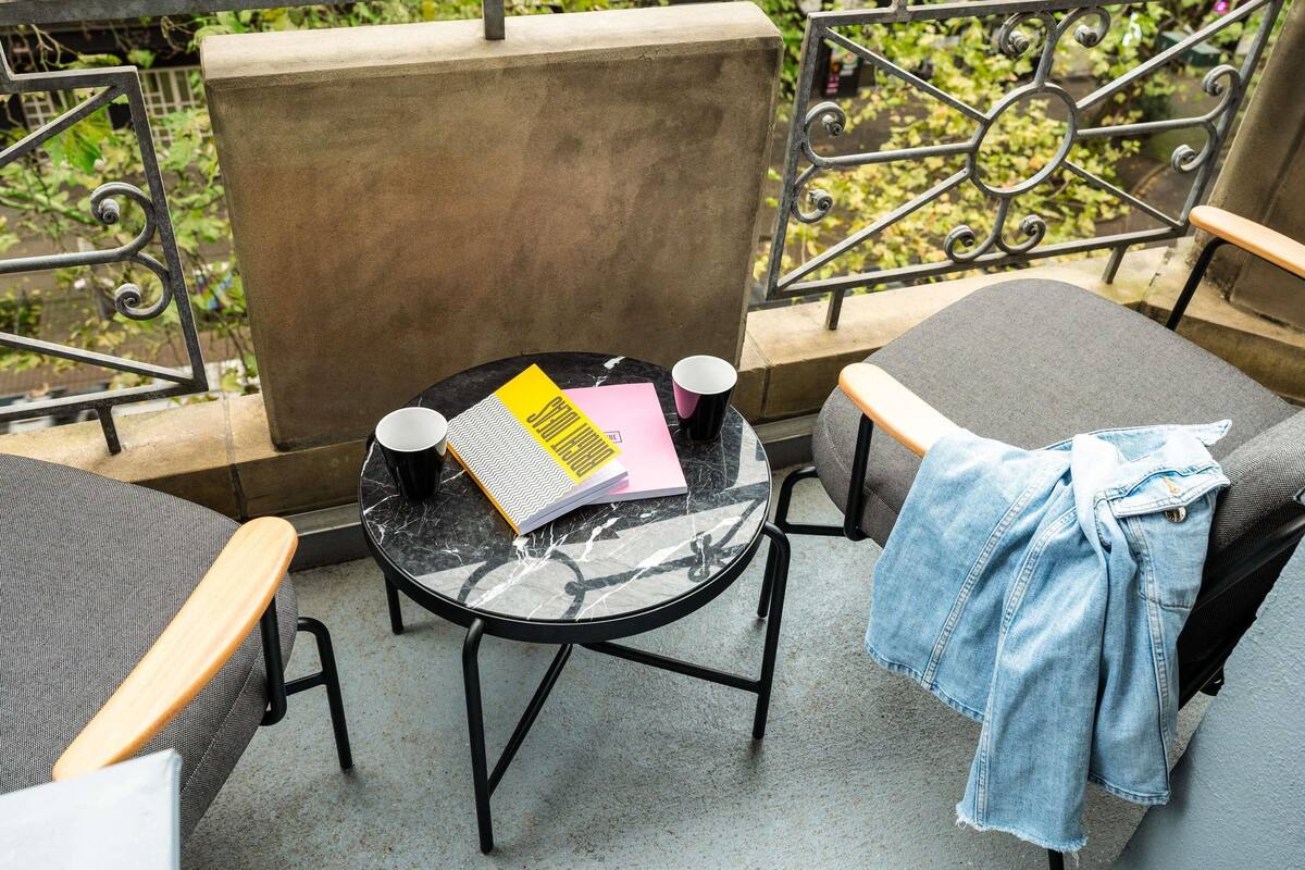 A balcony with a round table, two chairs, a metal railing, and a concrete block.