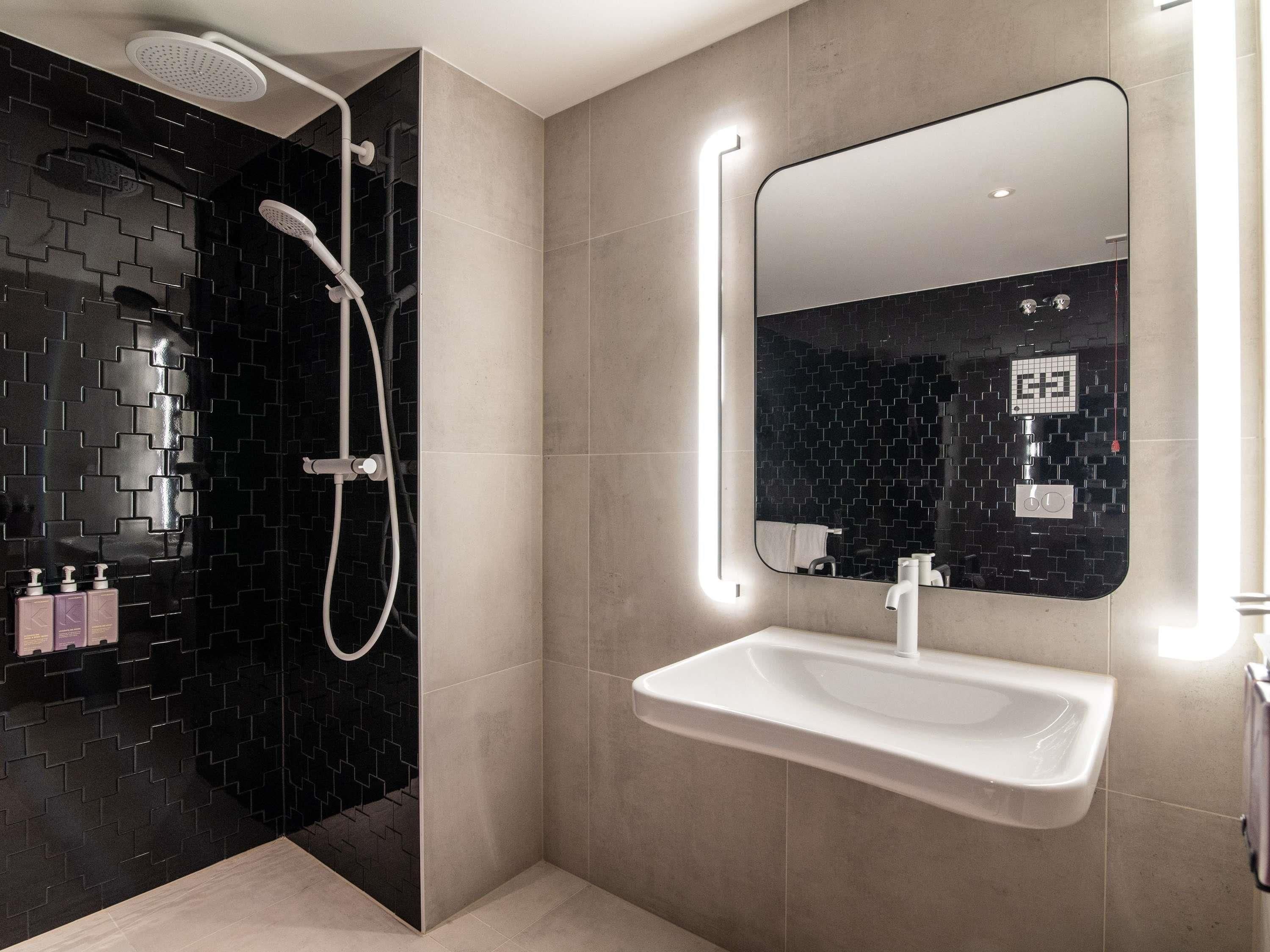 A modern bathroom with a black tiled shower area, a white sink, and a large mirror with a light strip.