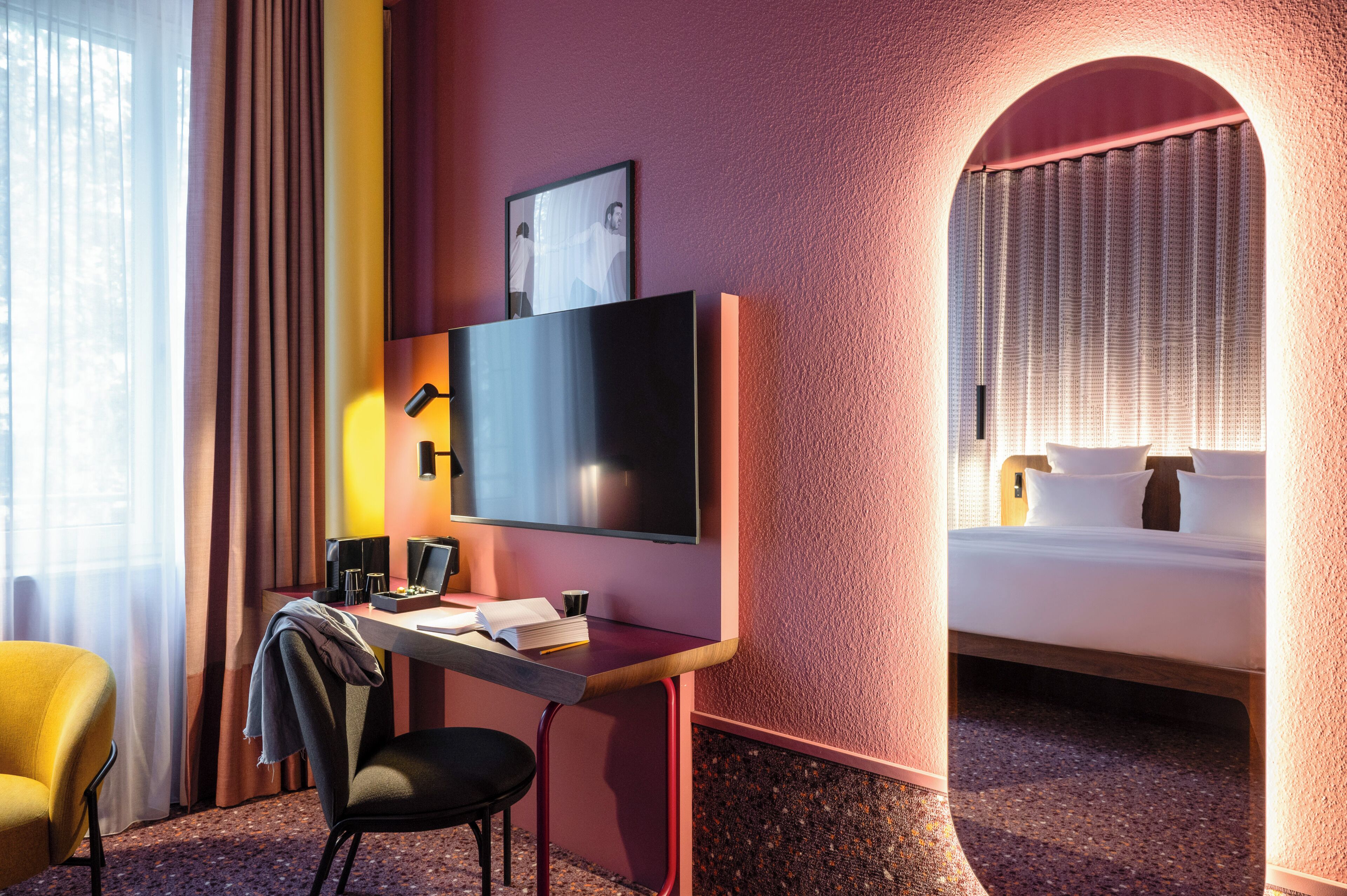 A hotel room with a bed, a desk with a chair, a television, and a window with curtains.
