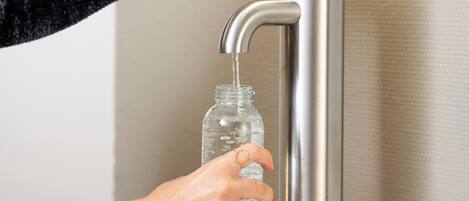 A hand filling a glass bottle from a modern faucet.