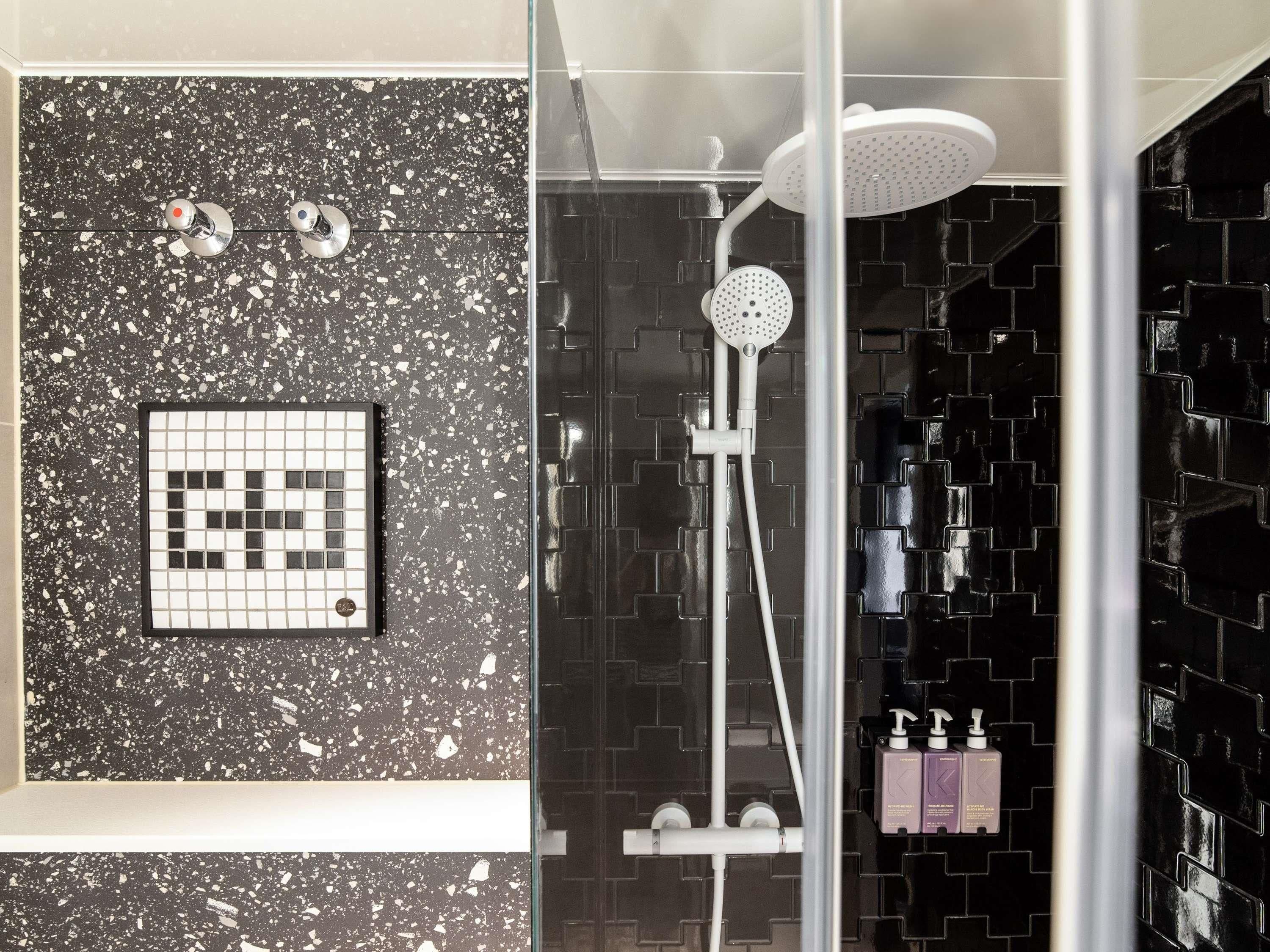 A modern bathroom with a black speckled tile wall, a glass shower enclosure, and a tiled shower area.
