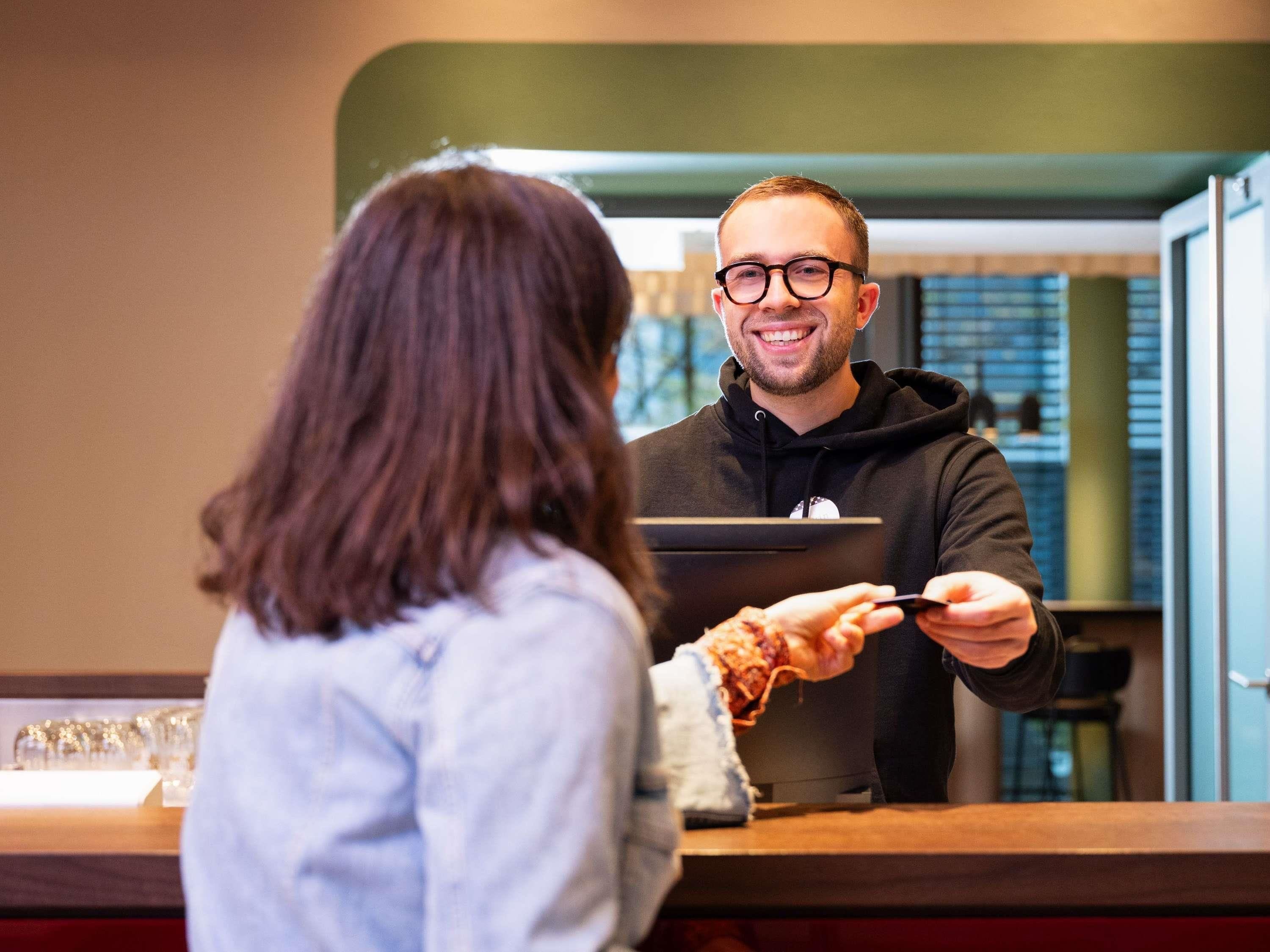 A person at a counter, possibly a hotel reception, with a laptop and a card.