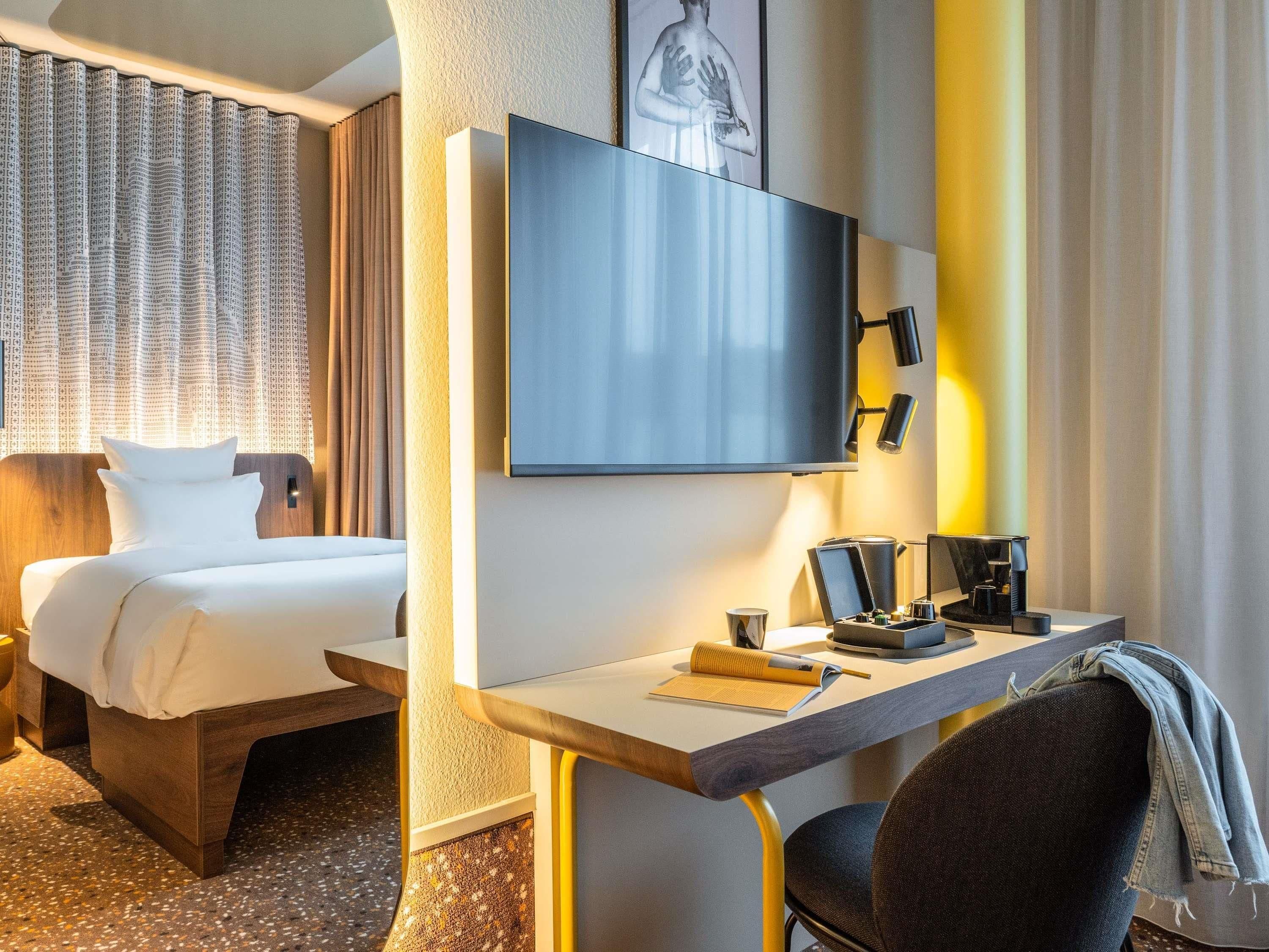 Habitación de hotel con cama, escritorio, silla, televisión de pantalla plana y cafetera.