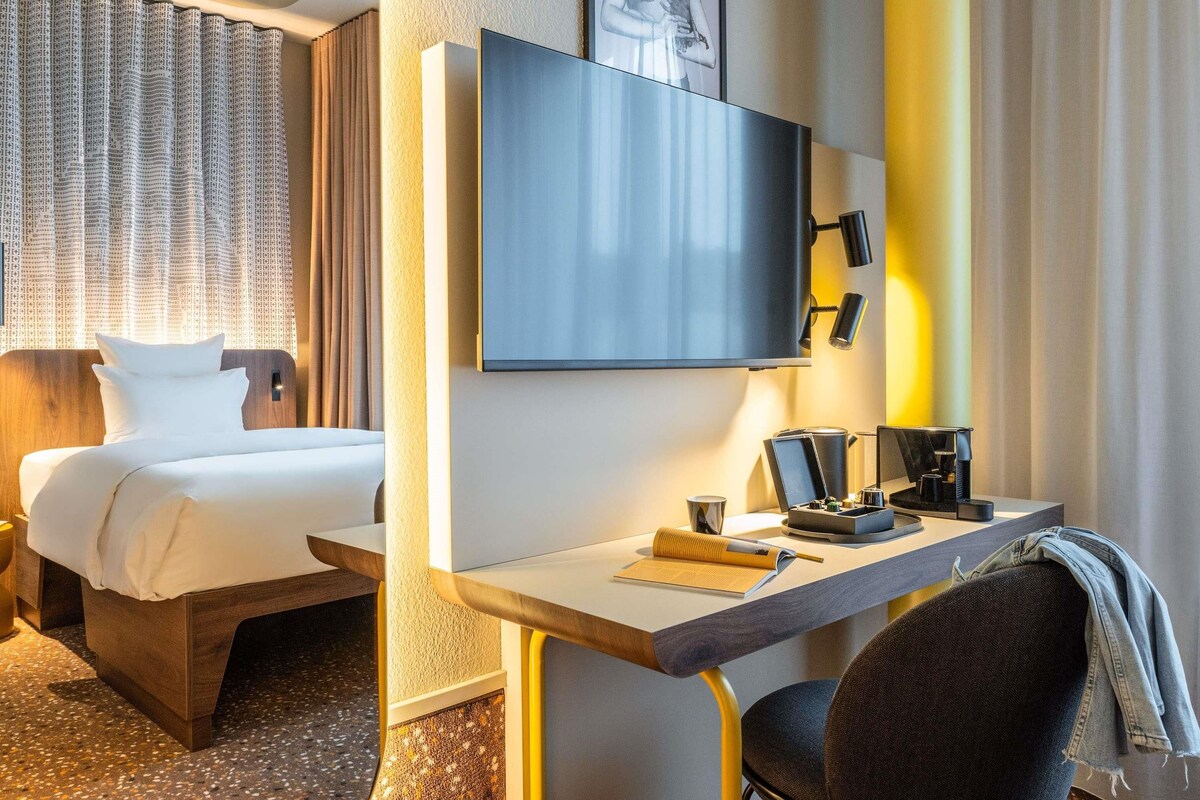 A hotel room with a bed, a desk with a chair, a flat-screen TV, and a coffee machine.