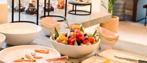 A buffet setup with various food items including fruits, meats, and a bowl of soup.