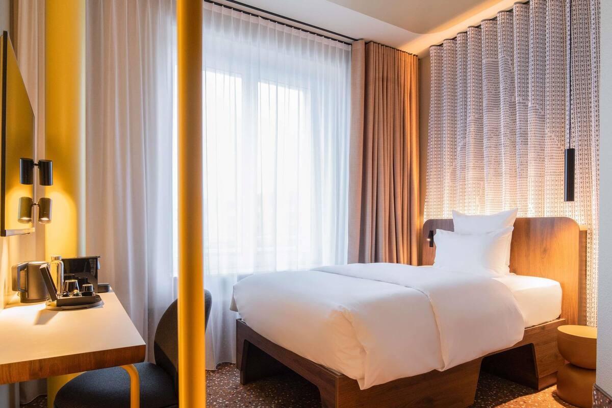 A hotel room with a bed, a desk, a chair, and a small table with a coffee maker.