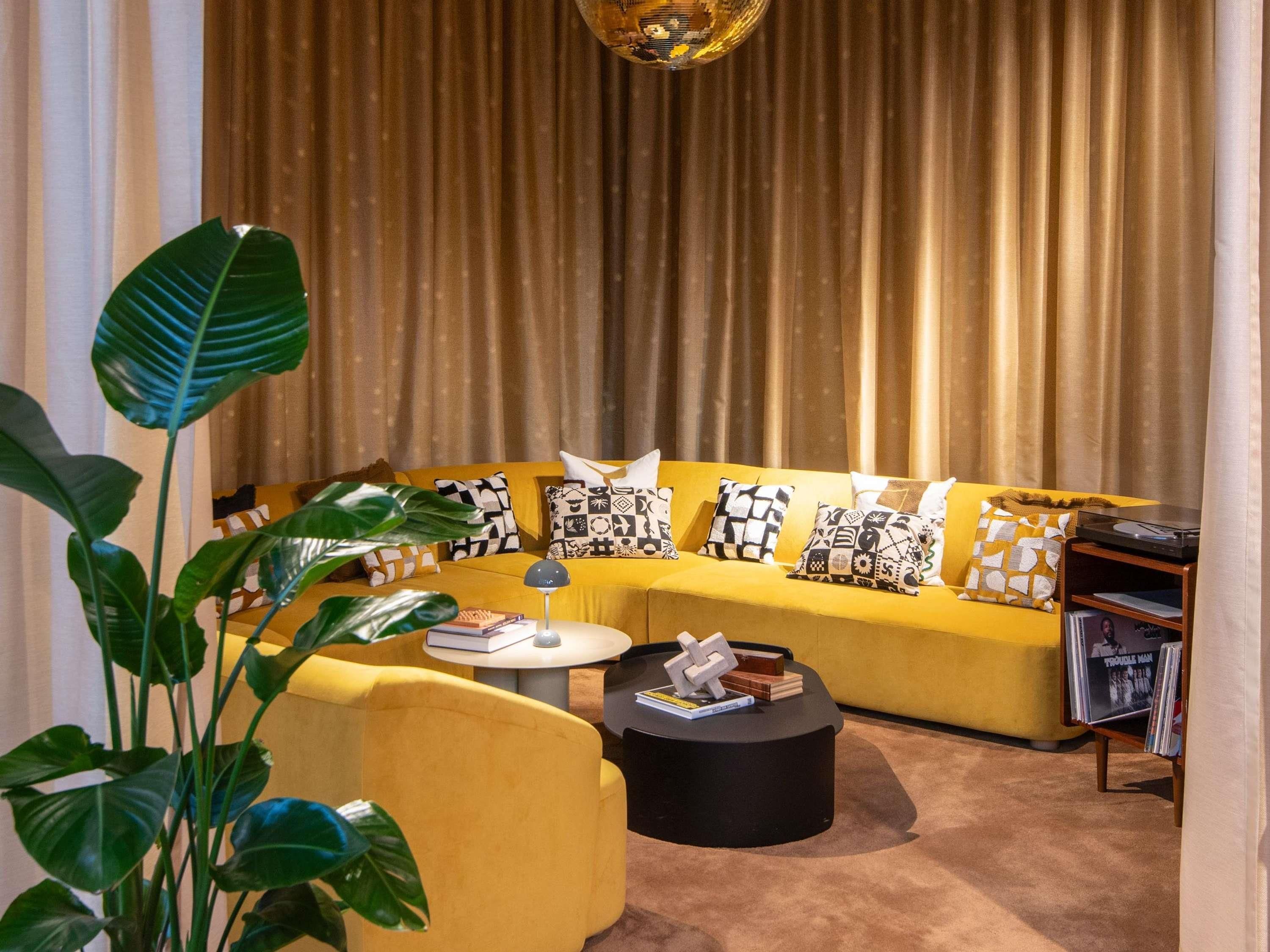 A living room with a yellow sofa, a black coffee table, and a plant.