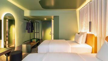 A hotel room with two beds, a desk, a chair, a coat rack, and a wardrobe.