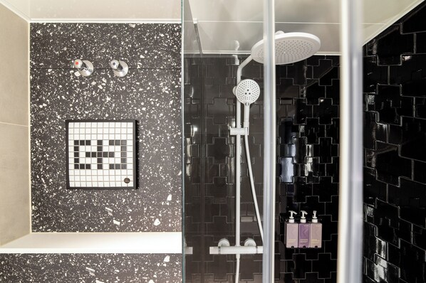 A modern bathroom with a shower, a tiled wall with a geometric pattern, and a glass partition. - TRIBE Düsseldorf (Düsseldorf)
