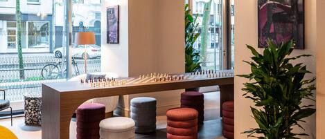 A modern interior with a foosball table, comfortable seating, and large windows offering a view of the street.