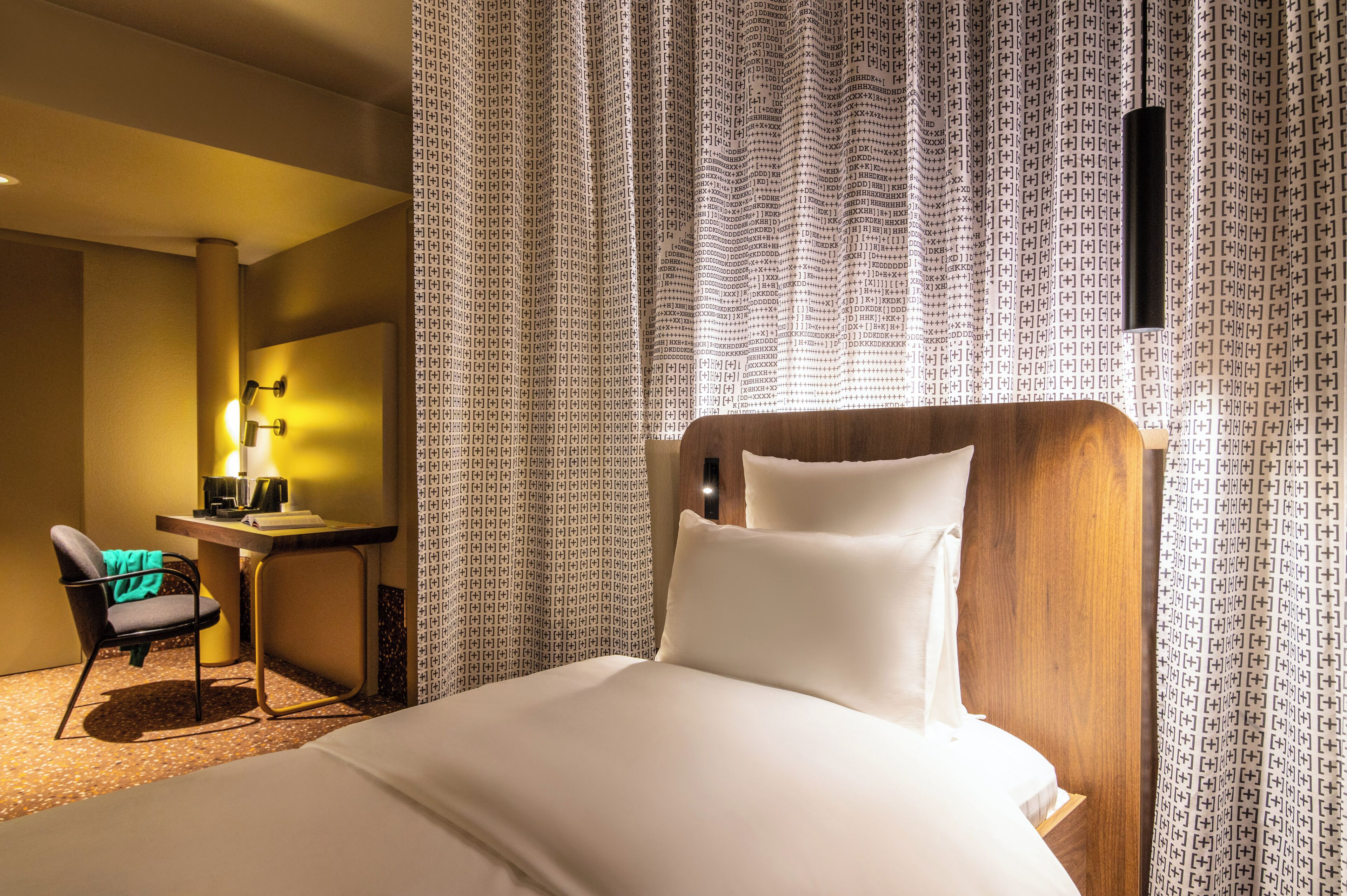 A hotel room with a bed, a desk, a chair, and curtains.