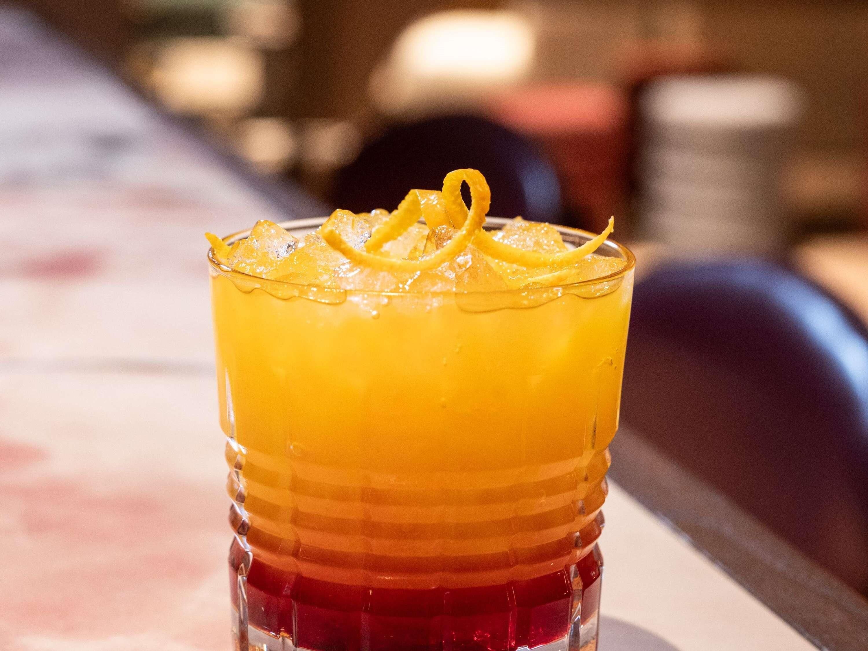 A glass with a layered drink, ice cubes, and a lemon garnish.