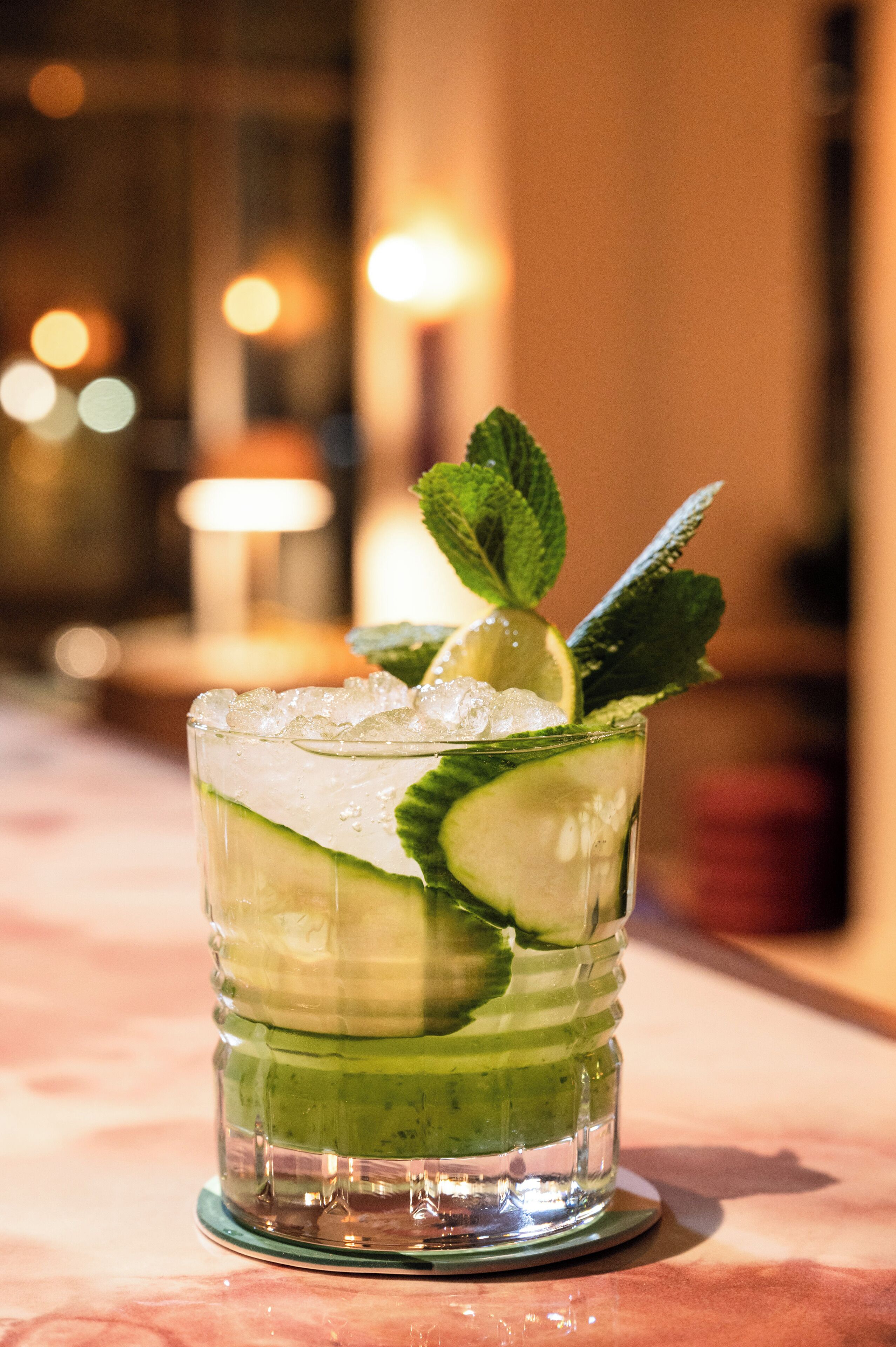 A glass of a green beverage with mint and lime, ice cubes, and a glass with a textured design.