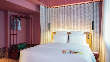 A neatly made bed with white linens, a magazine on the bed, and a suitcase on the floor.