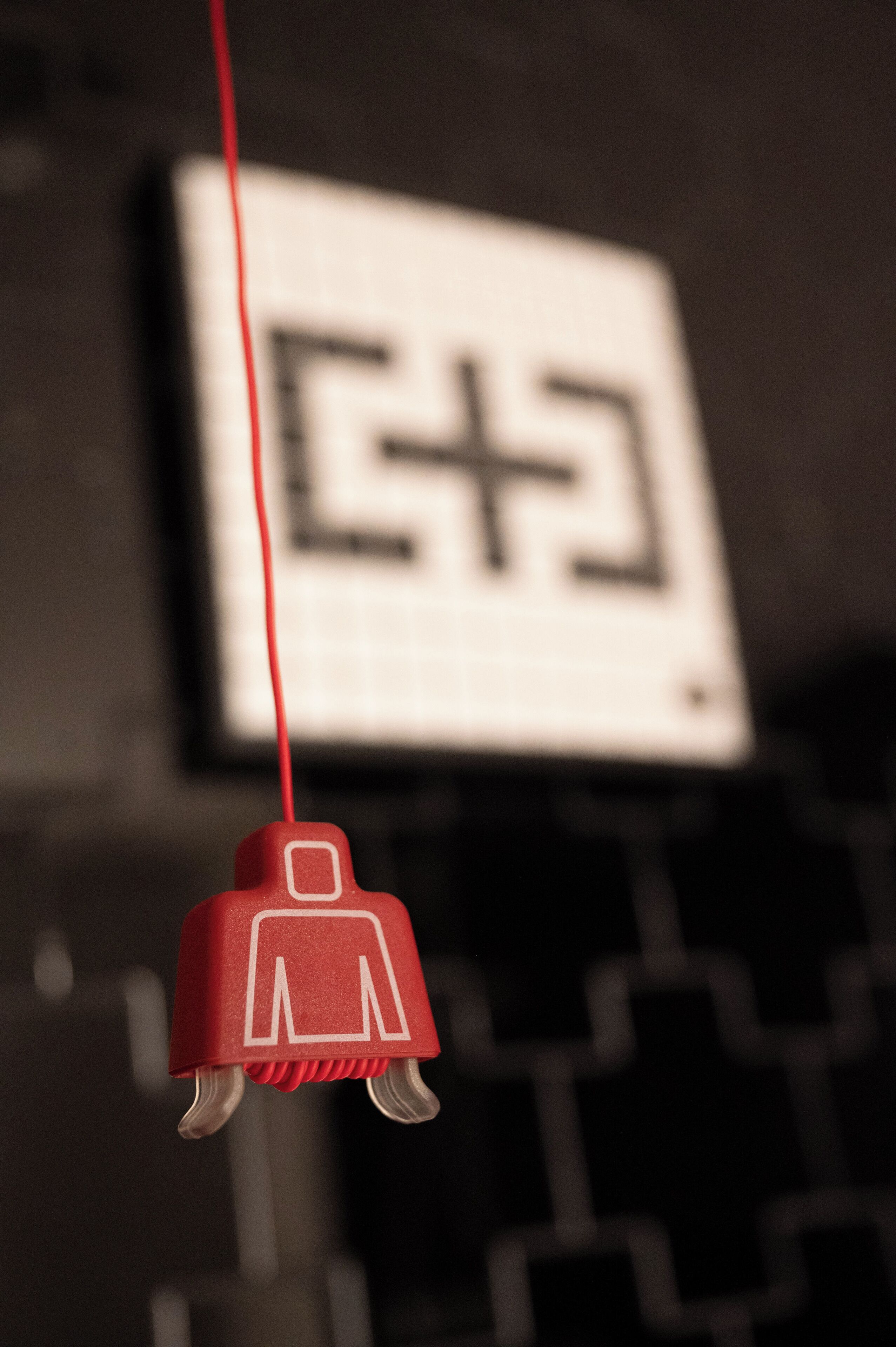 A close-up of a red object with a white square and a plus sign, hanging against a blurred background.