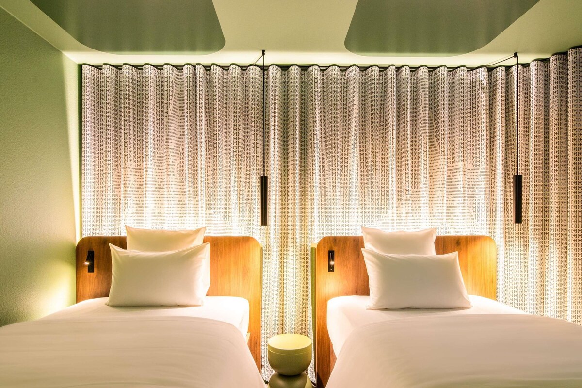 A hotel room with two beds, a small round table, and curtains with a pattern.