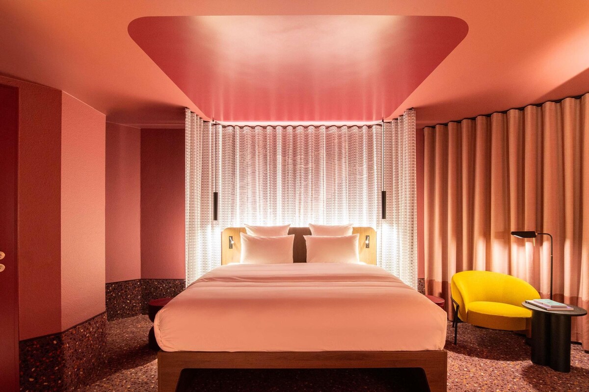A hotel room with a large bed, a yellow armchair, and a small side table.