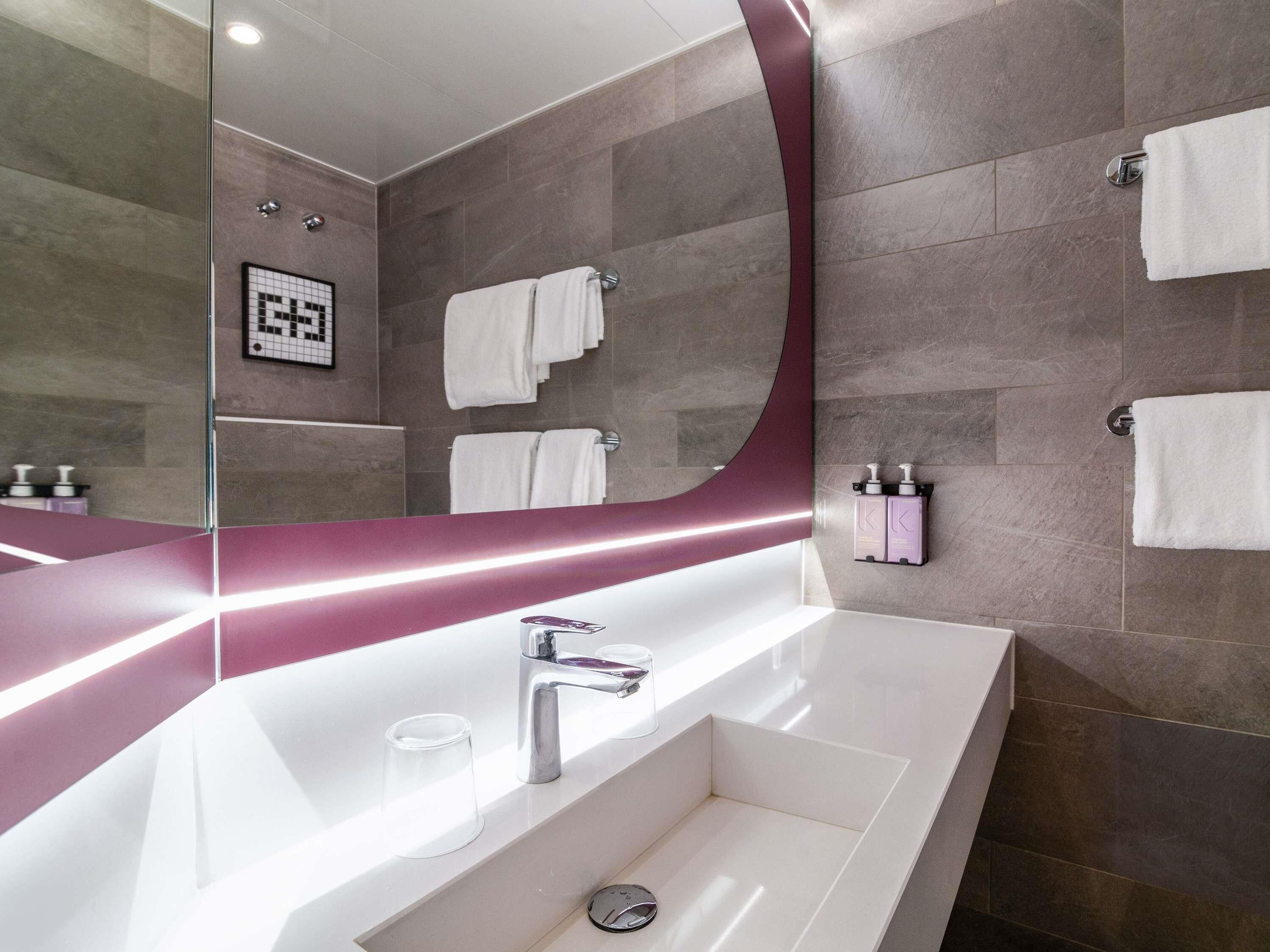 Een moderne badkamer met een grote spiegel, een witte wastafel en diverse handdoeken.