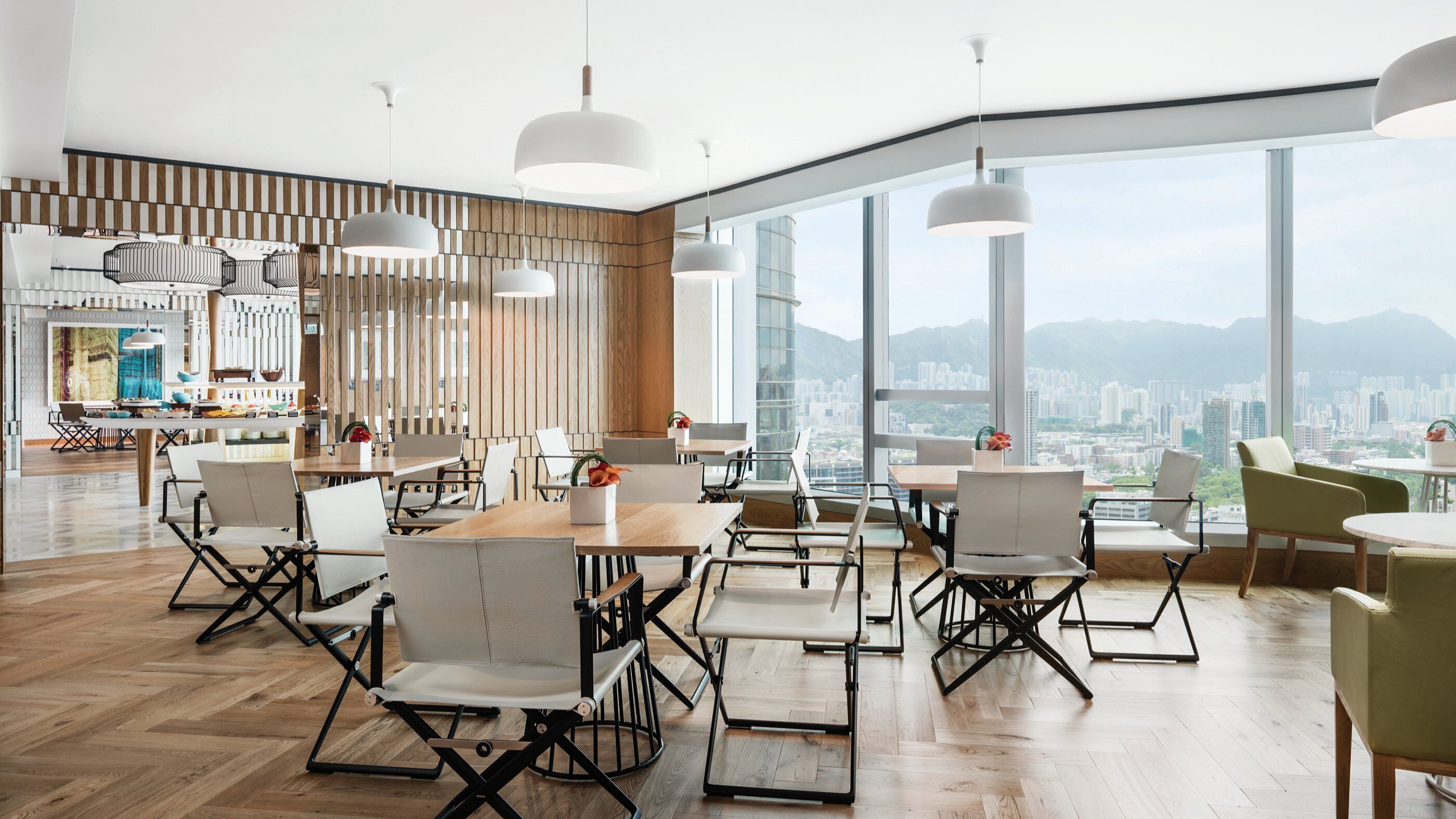 A modern dining area with a high ceiling, large windows offering a city view, and contemporary furniture.
