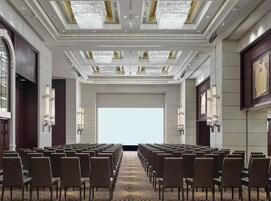 A conference room with rows of chairs, a large screen, and a chandelier.