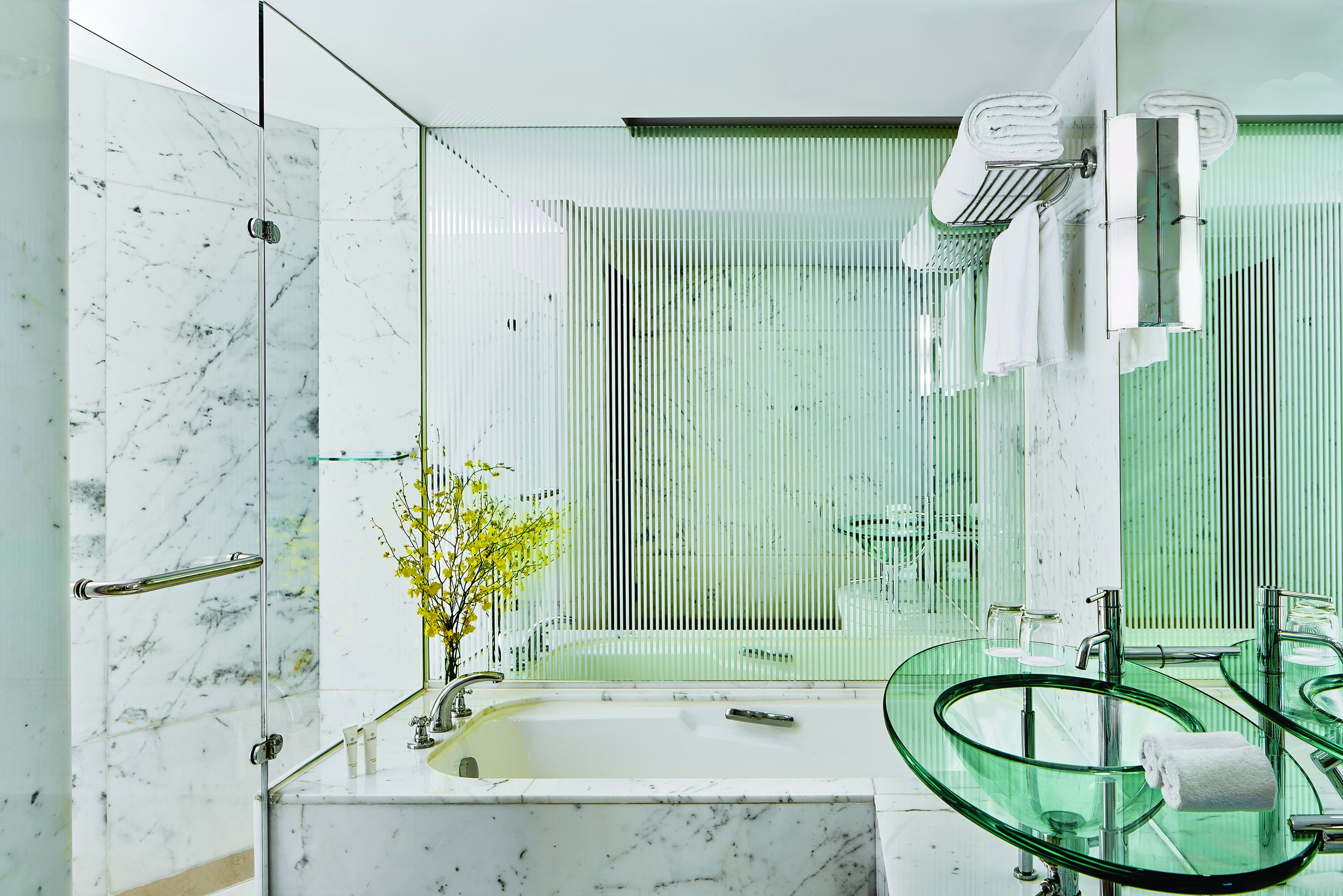 A modern bathroom with a glass-enclosed shower, a glass sink, and a large mirror.