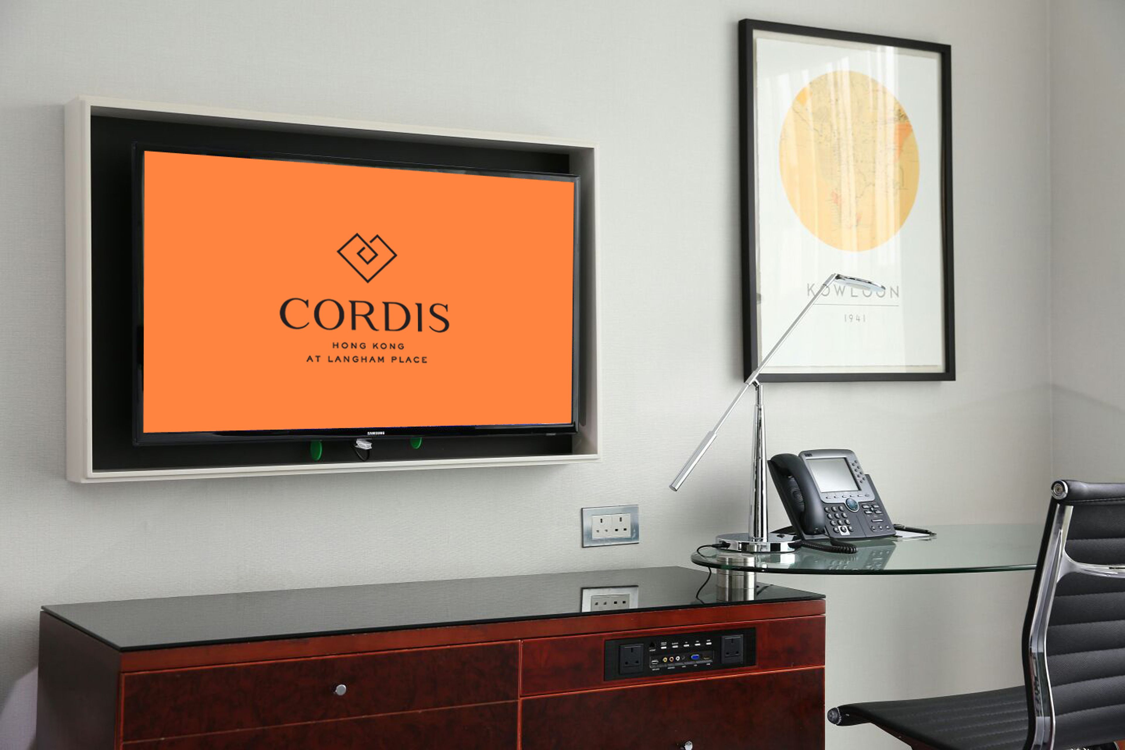 A modern office space with a large screen displaying "CORDIS" and "HONG KONG AT LANGHAM PLACE".