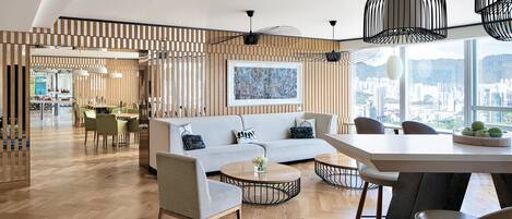 A modern living room with a sofa, chairs, a dining table, and a city view through large windows.