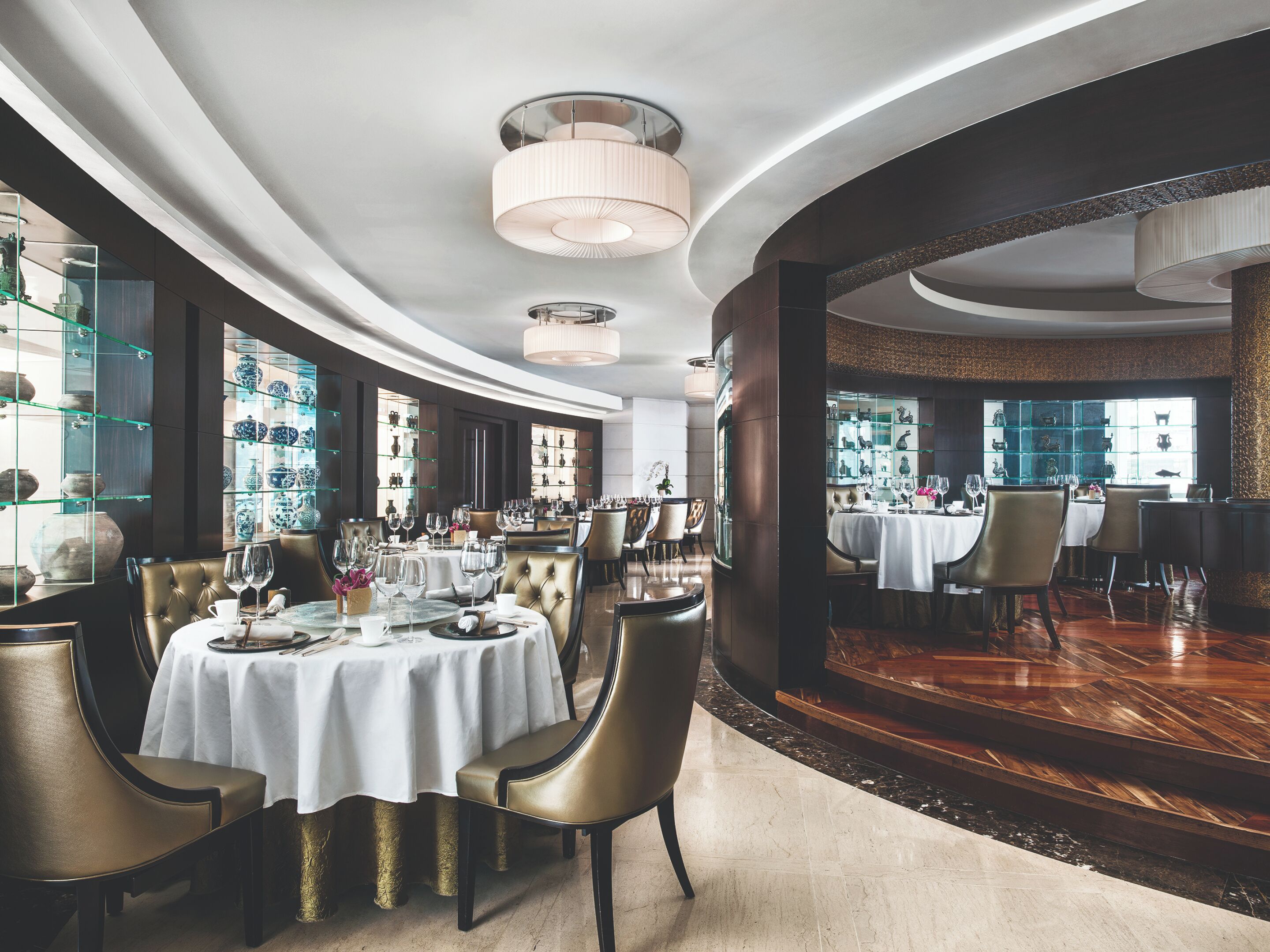 A luxurious dining area with round tables, elegant chairs, and a view of a bar area.