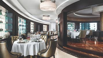 A luxurious dining area with round tables, elegant chairs, and a view of a bar area.