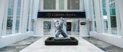 Un hall d’hôtel moderne, agrémenté d’une sculpture centrale, de grandes fenêtres et d’une enseigne indiquant « Cordis Hotel ».