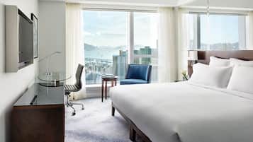 A hotel room with a large bed, a desk with a chair, a small table, and a view of the city.