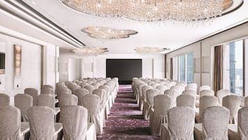 A conference room with rows of chairs, a large chandelier, and a carpeted floor.