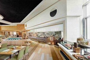 Un restaurant moderne doté d’un long comptoir, de plusieurs espaces de restauration et d’une cuisine visible au fond de la salle.