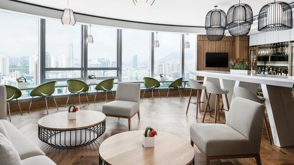A modern lounge area with a city view, round tables, green chairs, and a bar with a wooden backdrop. - Cordis, Hong Kong (Kowloon)