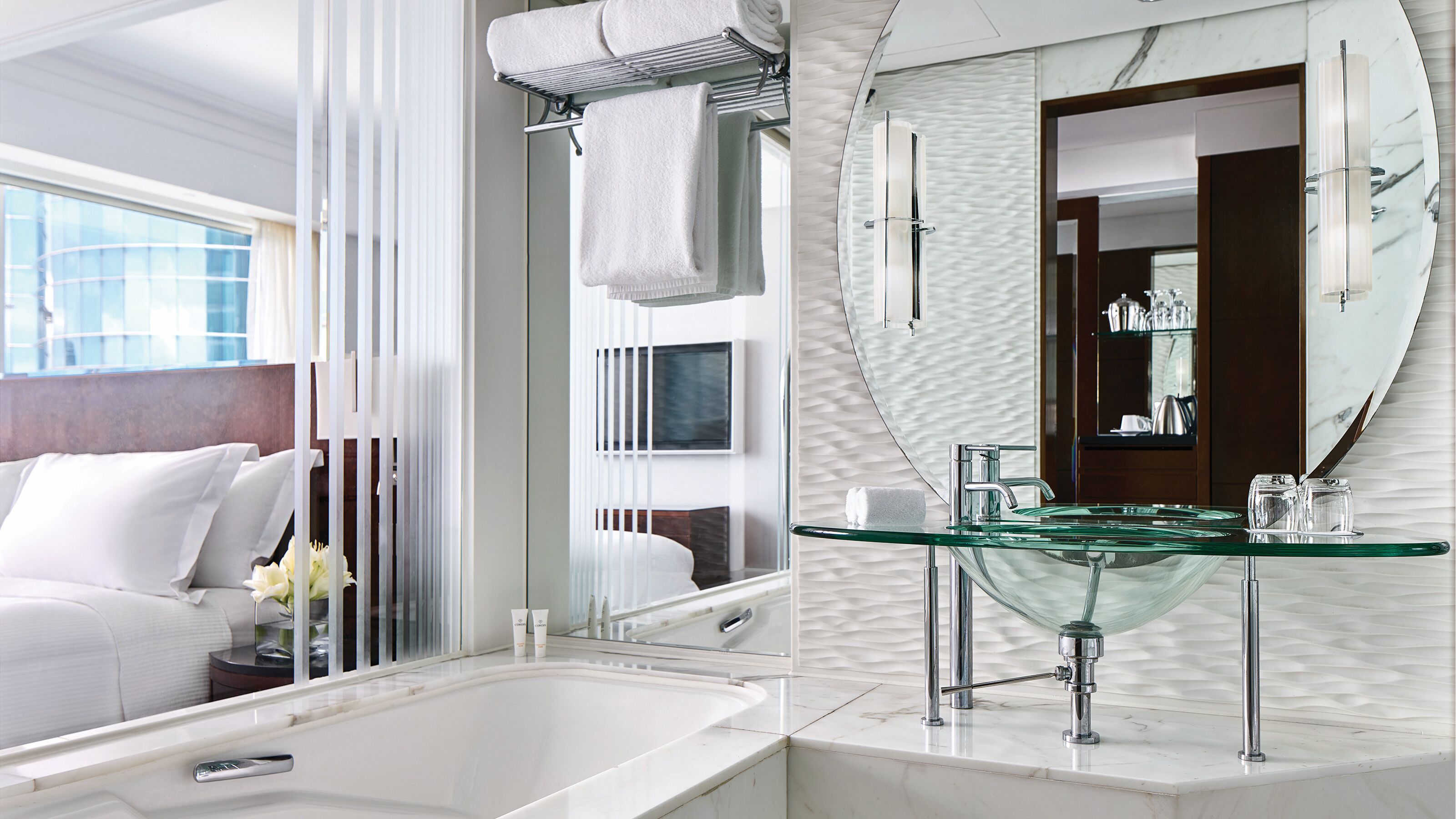 A modern bathroom with a glass sink, a bathtub, and a large mirror.