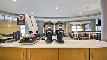 A coffee station with two coffee makers and a stack of disposable cups.