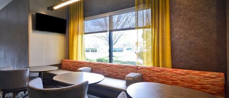 A modern hotel room with a large window, a flat-screen TV, and a seating area with sofas and tables.
