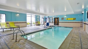 Una piscina con solárium empedrado, sillas de descanso y un puesto de socorrista.