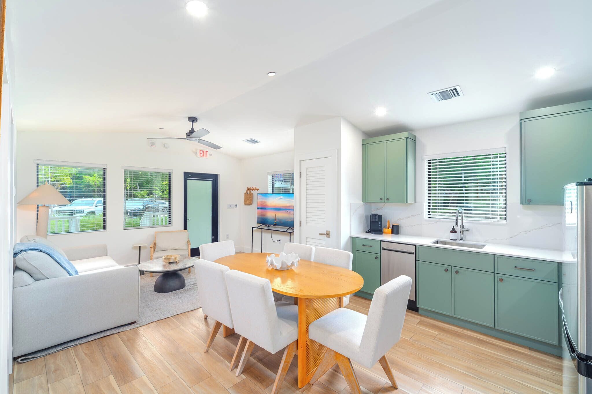 A modern kitchen with green cabinets, a dining area with a round table and chairs, and a ceiling fan.