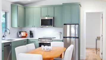 Una cocina moderna con gabinetes color turquesa, electrodomésticos de acero inoxidable y una mesa de comedor de madera.