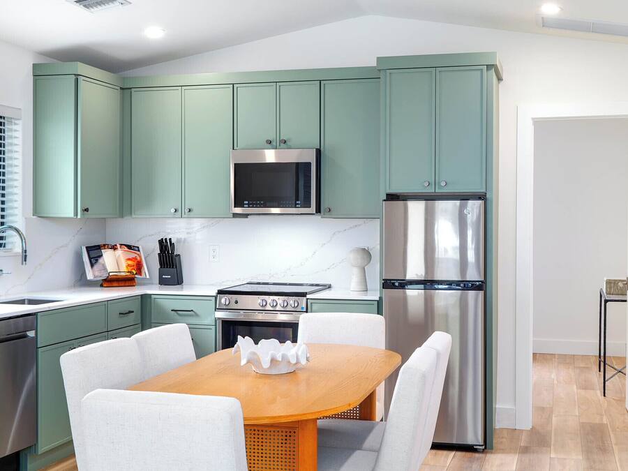 Una cocina moderna con gabinetes color turquesa, electrodomésticos de acero inoxidable y una mesa de comedor de madera.