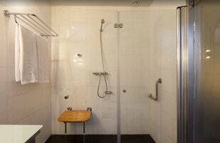 A shower area with a glass door, a towel rack, and a wooden stool.
