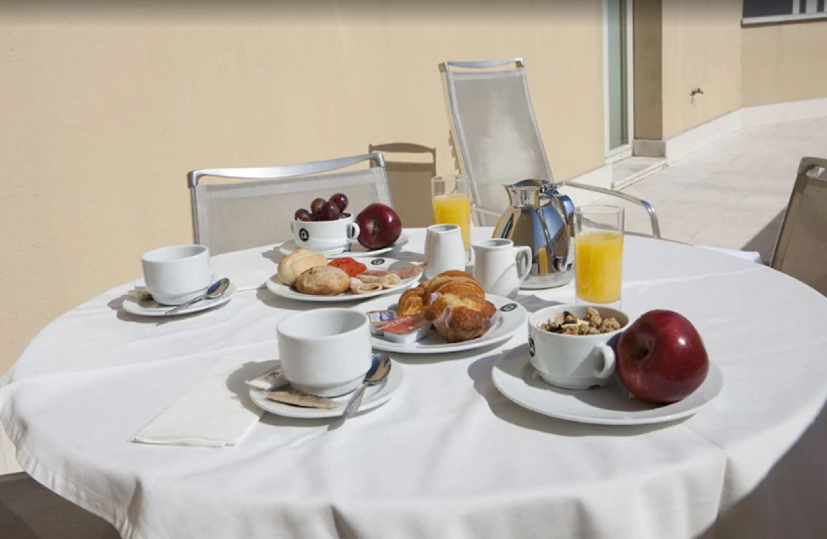 A breakfast table set with croissants, fruits, and beverages on a white tablecloth.