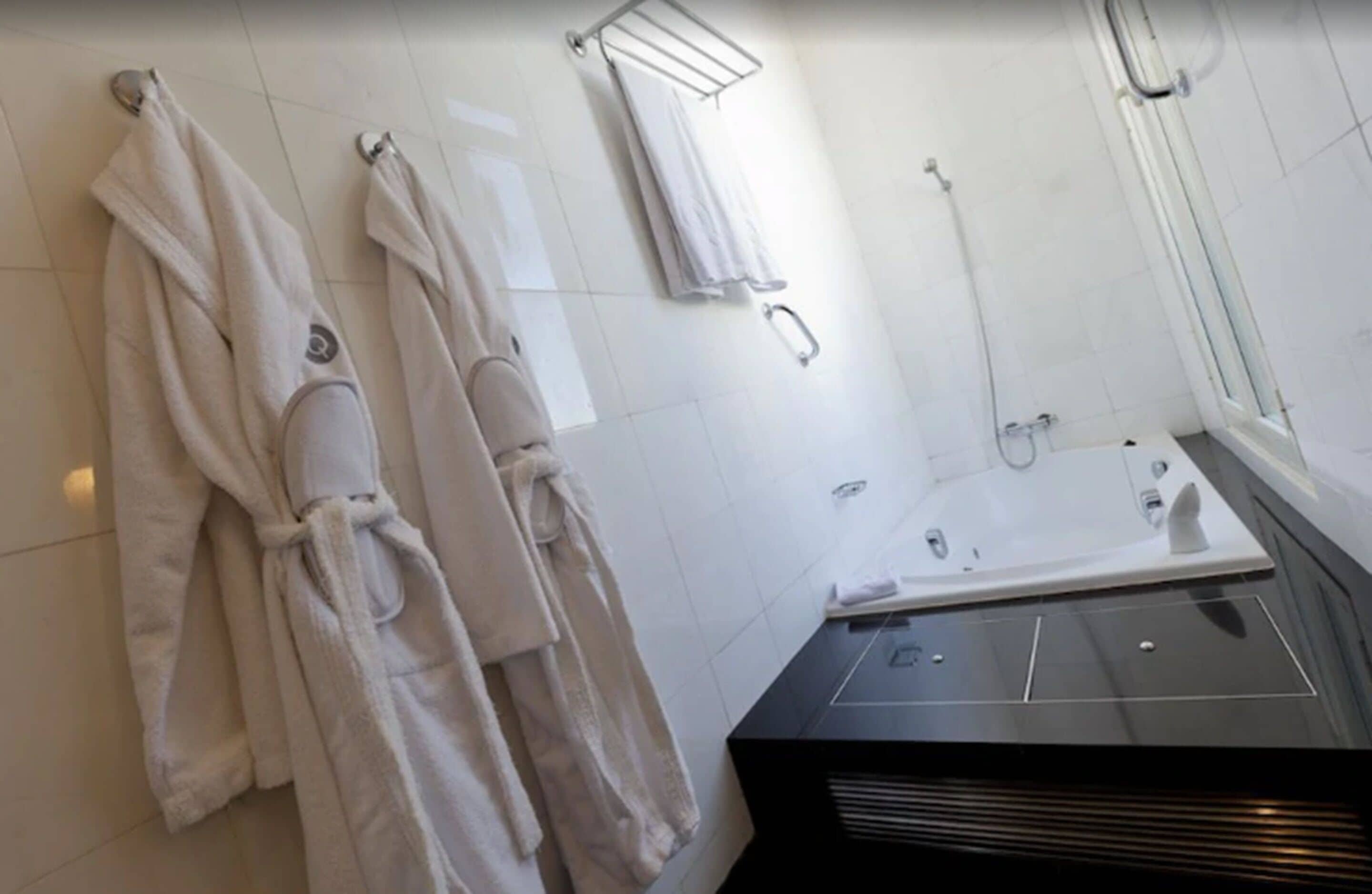 Un baño moderno con dos toallas blancas colgadas en ganchos, un box de ducha de vidrio y un lavamanos negro con un espejo encima.