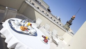 Zona de comedor en la azotea con una mesa dispuesta para el desayuno, que incluye cruasanes, frutas y bebidas.