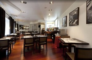 A restaurant with multiple tables and chairs, a kitchen area in the background, and framed artwork on the walls. - Hotel Quatro Puerta Del Sol (Madrid)