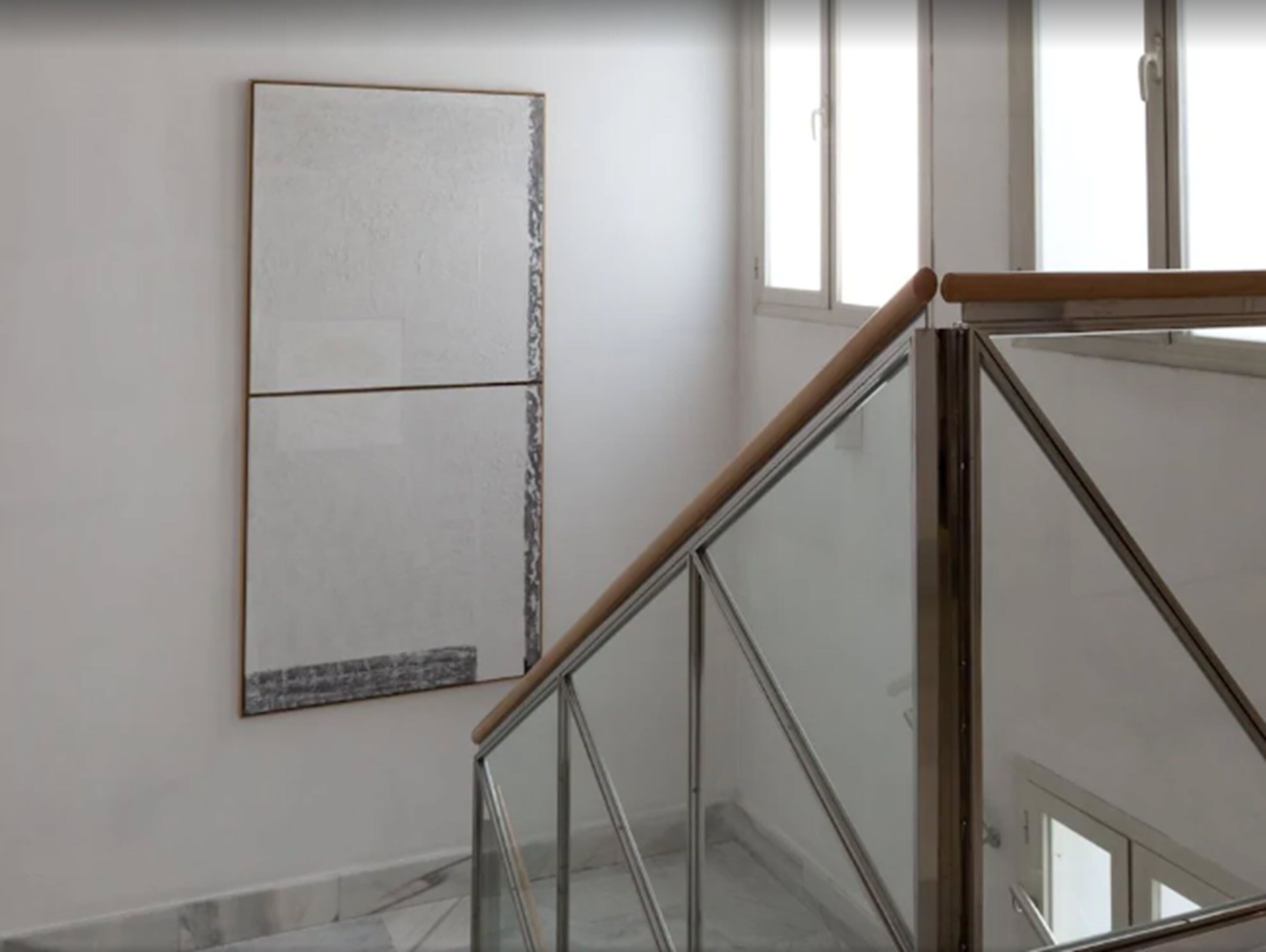 Una escalera con barandillas de vidrio y una pared lisa con un cuadro abstracto de gran tamaño.