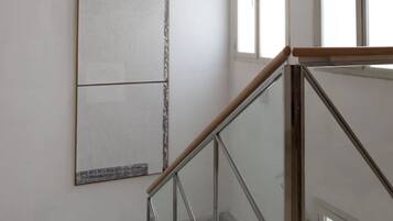 Una escalera con barandillas de vidrio y una pared lisa con un cuadro abstracto de gran tamaño.