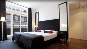 Habitación de hotel con una cama grande, una mesita de noche, un armario y una ventana con cortinas.